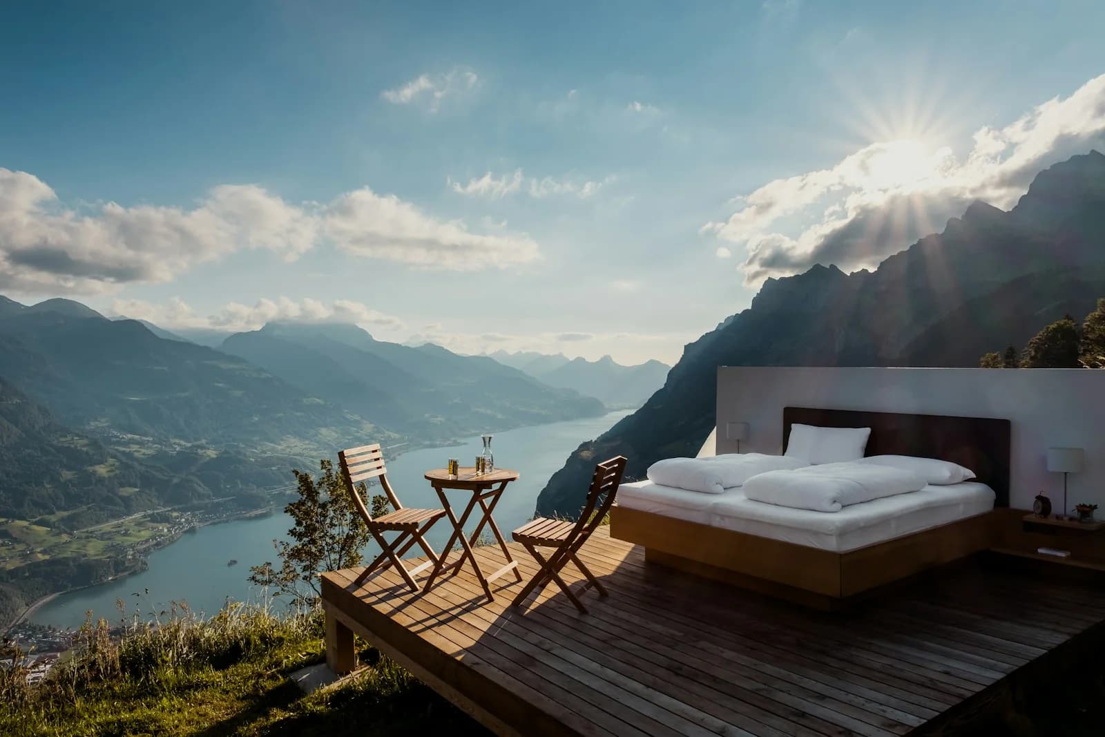 Open air luxury mountain deck with bed overlooking alpine lake and sun rays
